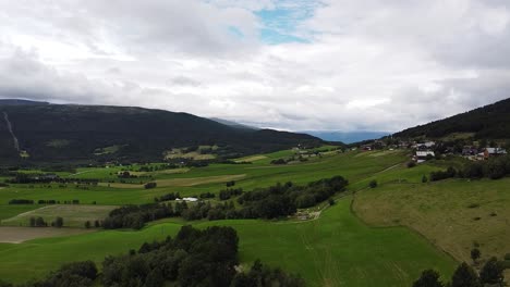 Drone-view-of-lush-green-fields-and-rolling-hills-in-Norway,-capturing-the-serene-landscape-under-a-partly-cloudy-sky