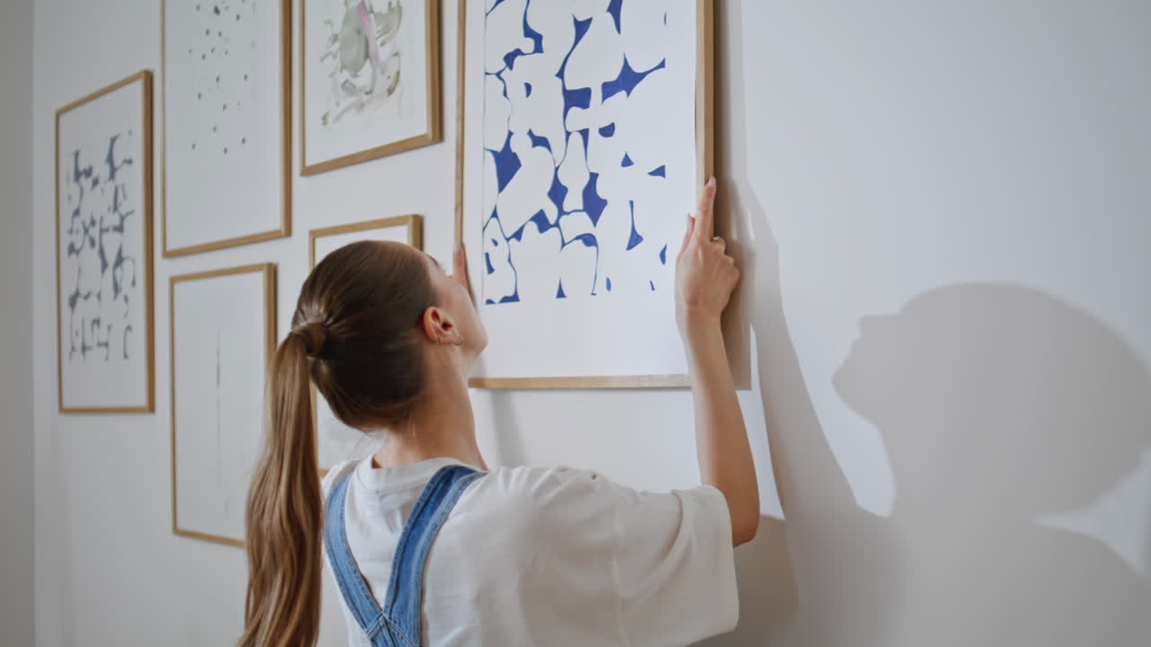 Girl hanging art picture on canvas at modern apartment during relocation closeup