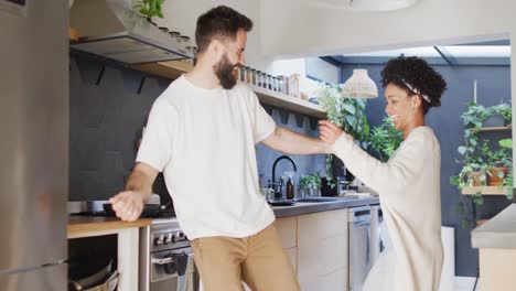 video de una feliz pareja diversa divirtiéndose bailando en la cocina