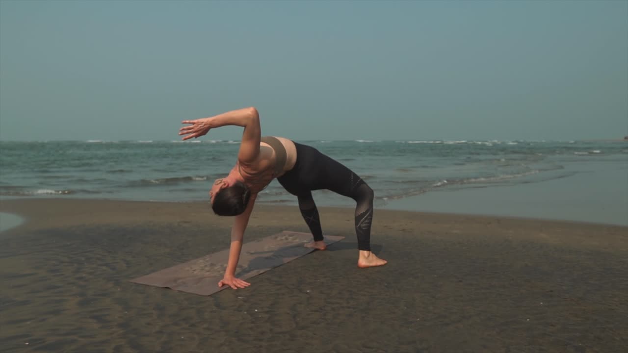 atleta practicando yoga en la playa al amanecer con olas lavando en tierra en el fondo
