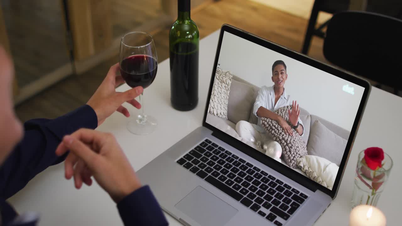Mixed race man sitting at table using laptop making video call with male friend