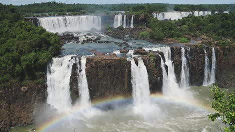 High-Above-Angle-View-of-Beautiful-Cliff-Edge-and-Rough-Waterfalls-Looking-Over-Colourful-Bright-Rainbow-Arch,-Beautiful-Rainbow-Colours-Formed-by-Waterfall-Splash-in-Iguacu-Falls,-Brazil