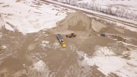 a wide drone shot showcases the full worksite as a truck and an excavator collaborate to transport and load sand efficiently.