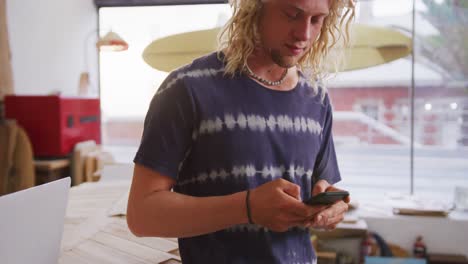 caucasian male surfboard maker standing in his studio and using his smartphone