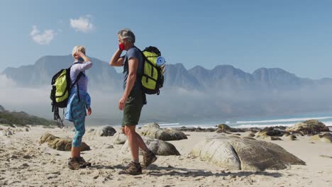 senior hiker couple wearing face masks with backpacks greeting each other by touching elbows