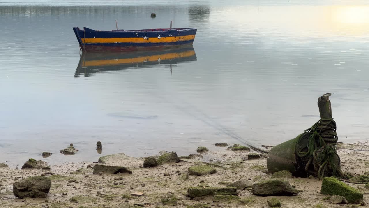 Serene boat floats on calm waters in Barbate, Andalusia, Spain. The shoreline features rocks and a buoy, creating a peaceful maritime landscape with reflections on the water