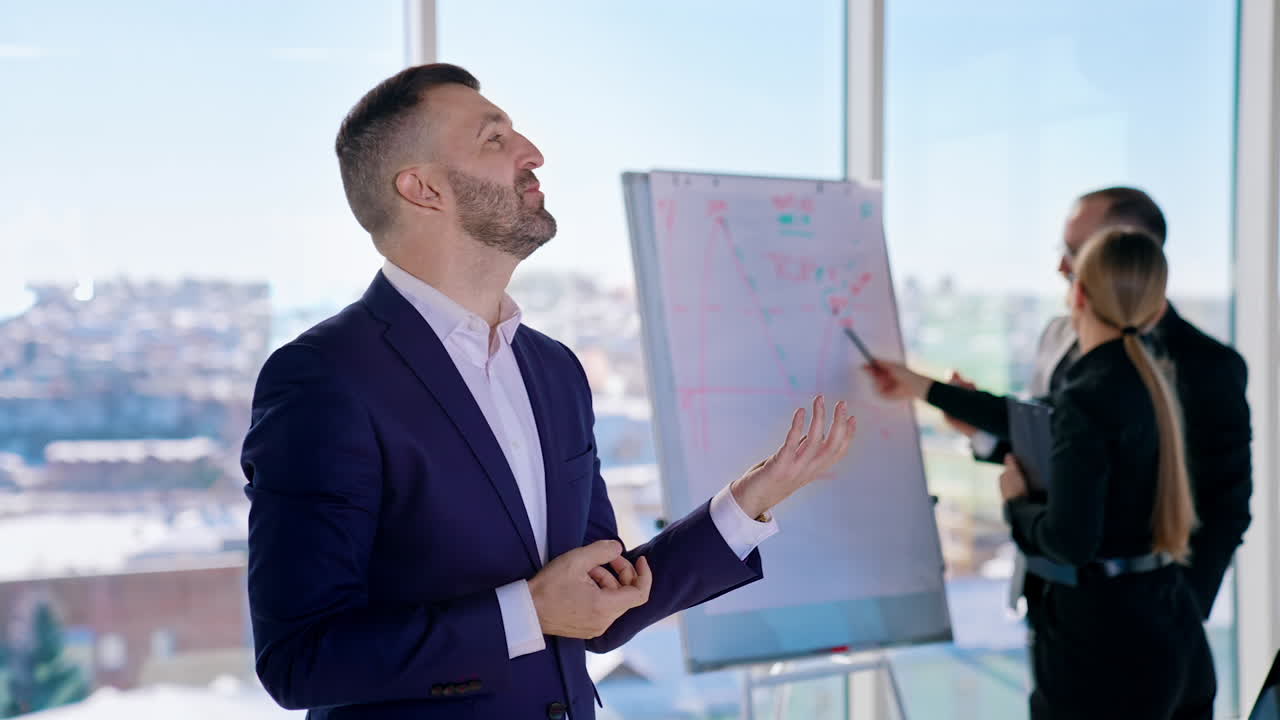 Entrepreneur in costume tells about his company. Successful businessman speaking about new project on the background of his colleagues working in office.