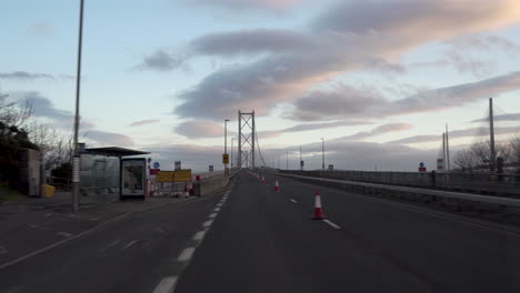 Toma-En-Movimiento-De-Un-Vehículo-Que-Cruza-Un-Puente-De-Carretera-Con-Una-Maravillosa-Luz-De-Puesta-De-Sol-Y-Nubes-En-Edimburgo,-Escocia