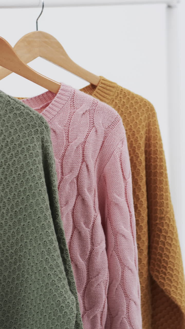 Vertical video of three multi coloured sweaters on hangers and copy space on white background