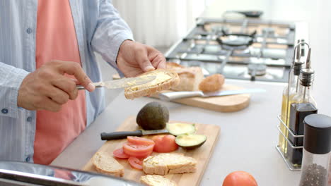 spreading butter on bread, man preparing breakfast with fresh vegetables in kitchen