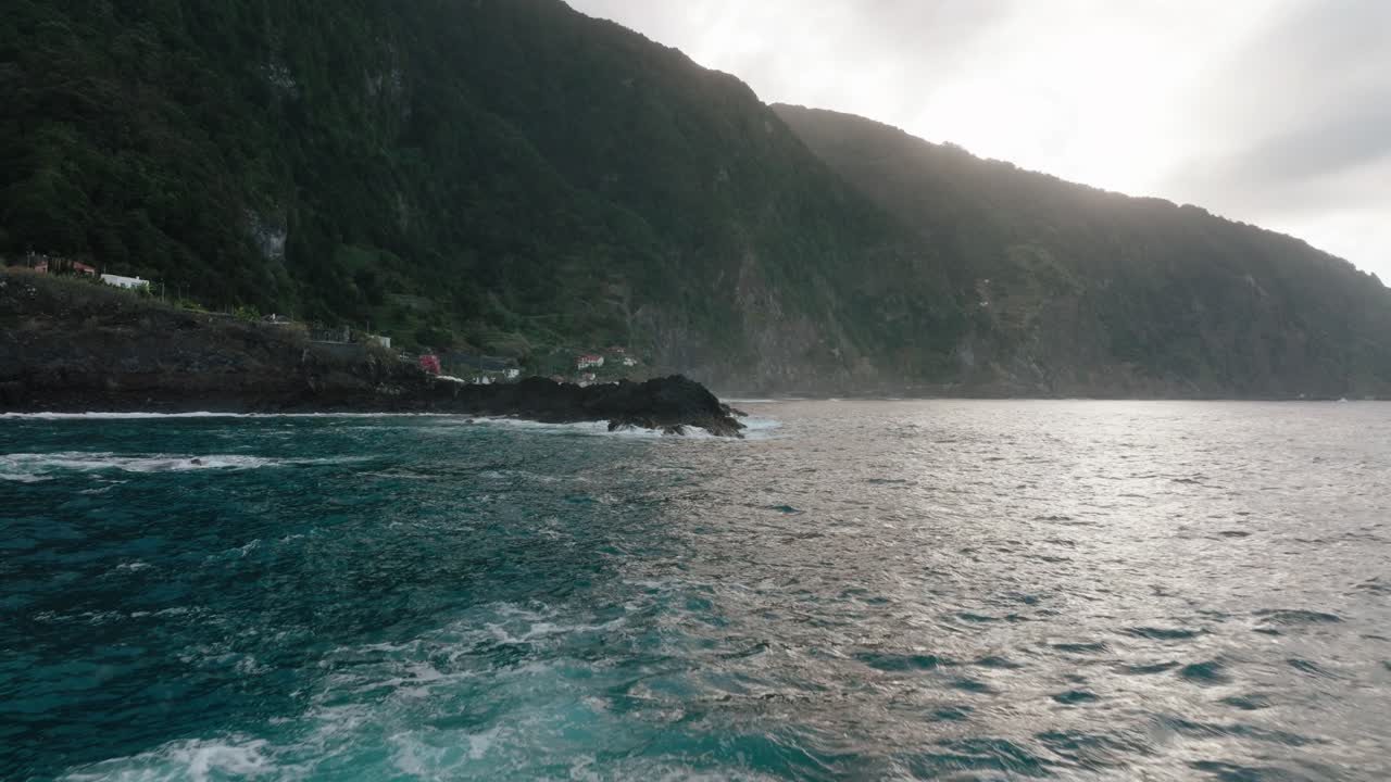 Aerial flyover of a man relaxing in volcanic natural pools beside the ocean in Seixal, Madeira at golden hour.
