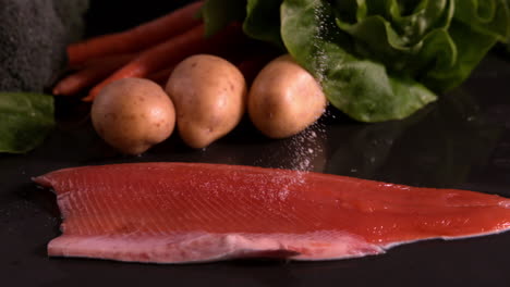 Hand-seasoning-trout-fillet-in-front-of-vegetable-selection