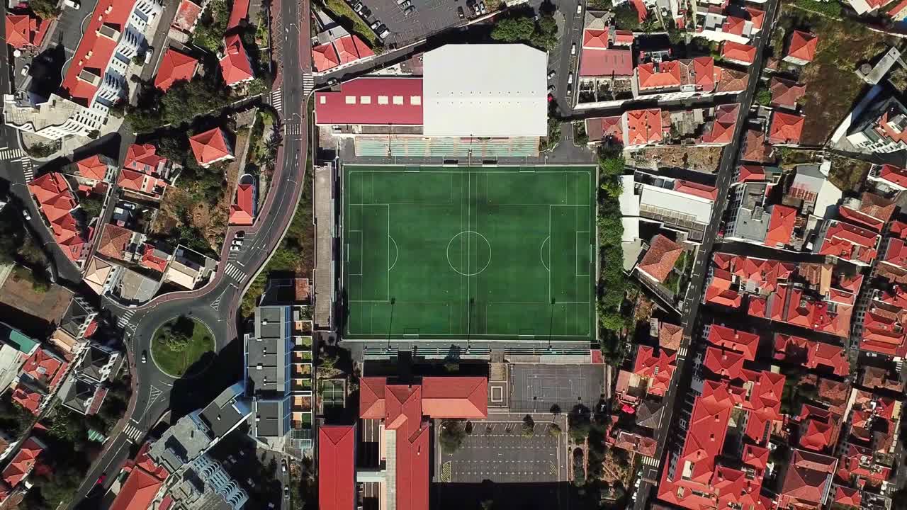 Aerial view of Adelino Rodrigues Field located in a residential area of Funchal, Madeira, showing the urban layout and surrounding buildings with red tile roofs, top down ascending drone shot