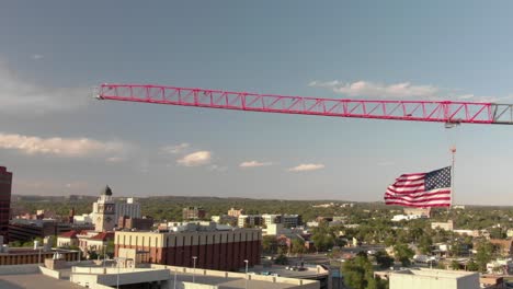 rotating aerial of construction crane in city with large american flag