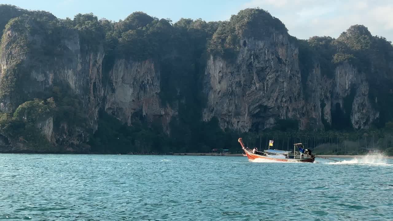 Crociera in barca a coda lunga su acque calme a Railay Beach, Krabi, con scogliere calcaree a picco che si ergono dalla costa e limpide condizioni tropicali che circondano la scena.