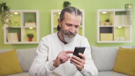 The-old-man-looking-at-the-phone-at-home-gets-emotional-and-sad.