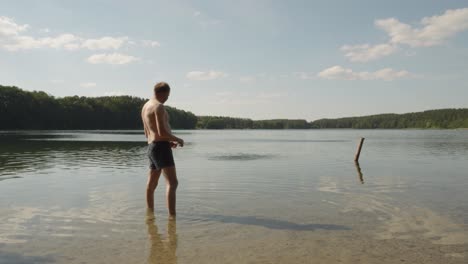 shirtless man skipping stones at glebokie lake in poland on a sunny day