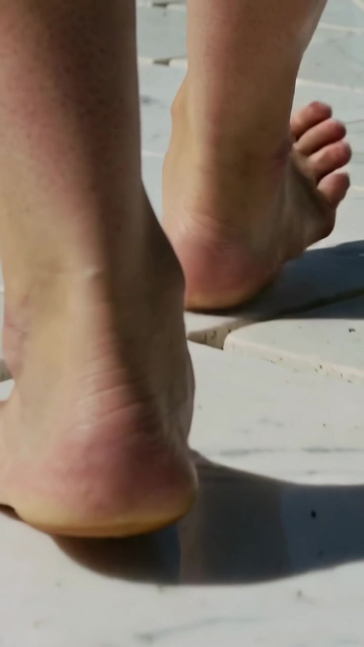 Video verticale: Telecamera che segue i piedi che camminano allontanandosi su una pedana bianca, con fessure e ombre.