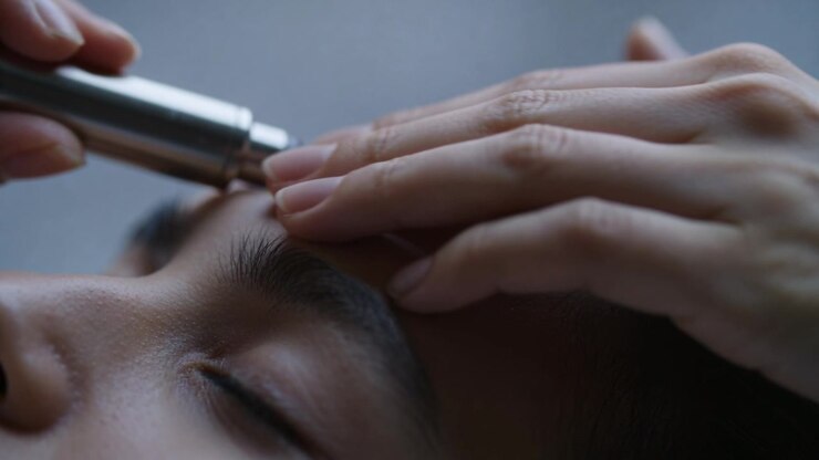 Approaching brow, device moving along right brow, hands pressing forehead at pillow for grooming