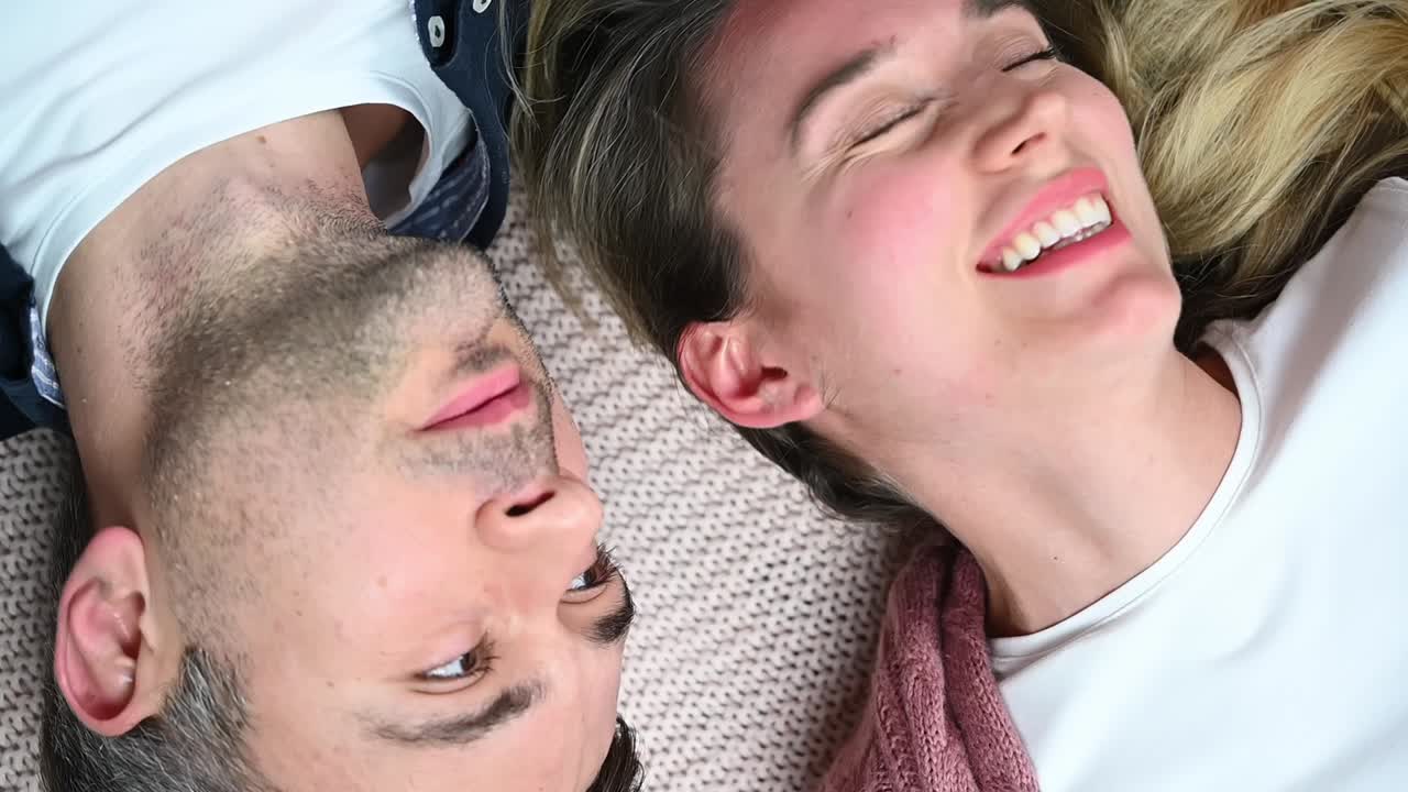 Young lovely couple relaxing head to head and talking on the bed. Woman smile and looking at the partner. Valentines day. Close up. Overhead cinematic shot. Relationships and feelings. Slow motion