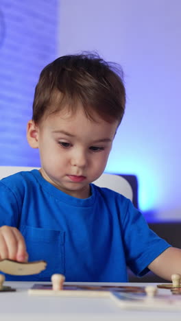 adorable little toddler in blue t-shirt playing peacefully at the desk. baby boy matching puzzle pieces. blurred backdrop. vertical video
