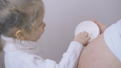 chica en suéter ayuda a la madre embarazada a aplicar loción en el vientre