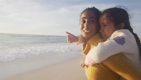 Glückliche-Hispanische-Mutter-Trägt-Huckepack-Tochter-Und-Blickt-Auf-Den-Sonnenuntergang-Am-Strand