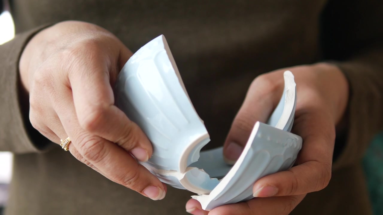 Close-up of Hands Trying to Piece Together a Broken Ceramic Bowl