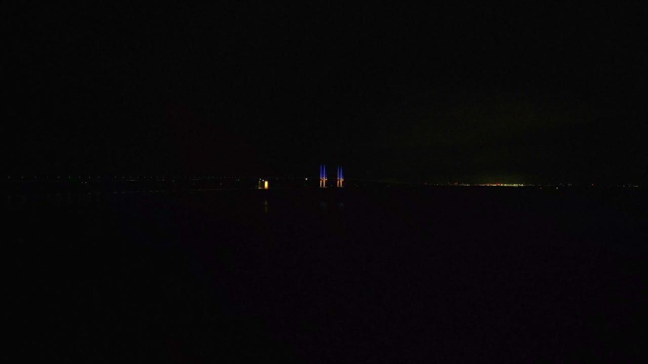 어둠 속에서 두 개의 파란색과 노란색 기둥이 빛나는 밤의 öresundsbron과 다리에서 운전하는 자동차