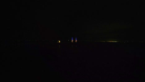 öresundsbron de noche con dos pilares azules y amarillos brillando en la oscuridad y autos circulando por el puente