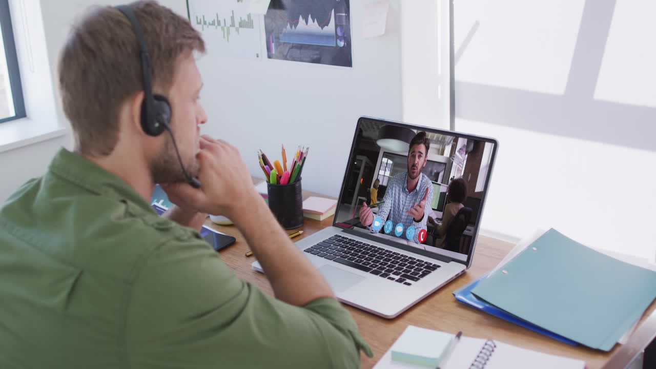 Kaukasisk mand med telefonheadset på har videoopkald med mandlig kollega på bærbar computer på kontoret