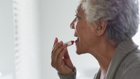 Mujer-Mayor-Afroamericana-Aplicando-Lápiz-Labial-Mientras-Se-Mira-En-El-Espejo-En-Casa