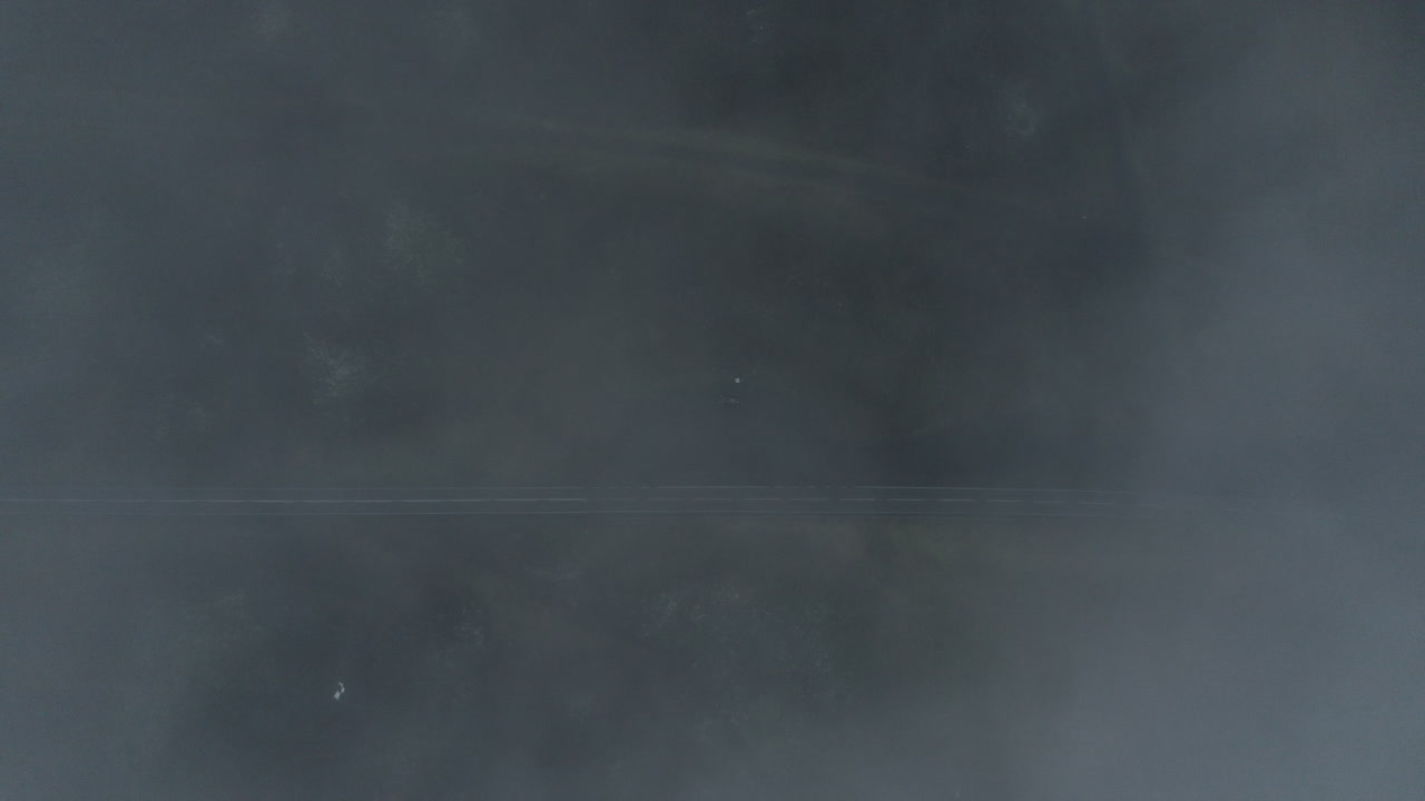 아래에 도로와 밴이 있는 북부 아이슬란드의 안개가 자욱하고 어두운 풍경 속으로 떠다니고 있습니다.