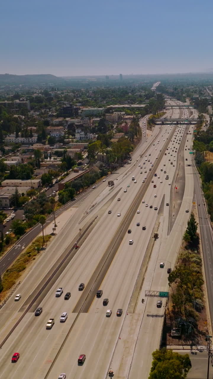 Multi-lane highway with numerous cars going through the big city. Sunny picture of Los Angeles from aerial view. Vertical video
