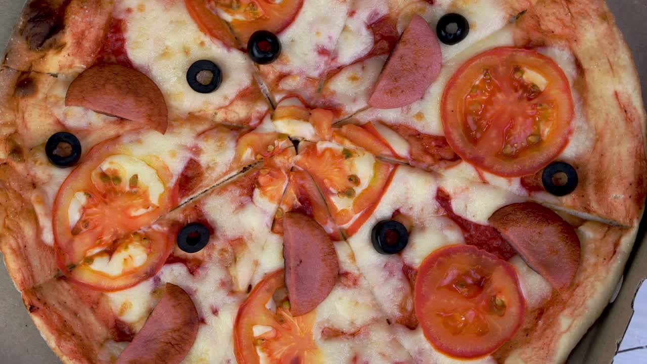 토마토, 소시지, 모차라, 올리브가 들어있는 신선한 둥근 피자는 천천히 회전합니다.