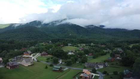 Aerial-shot-of-a-neighborhood-flying-toward-mountains-with-clouds