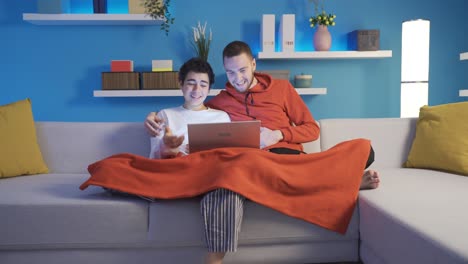 hermanos felices viendo películas de comedia juntos en casa usando portátiles, navegando por las redes sociales.