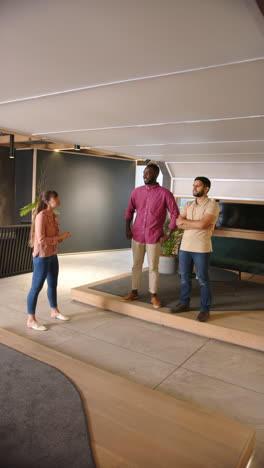 vertical video: discussing project, diverse business team standing and talking in modern office