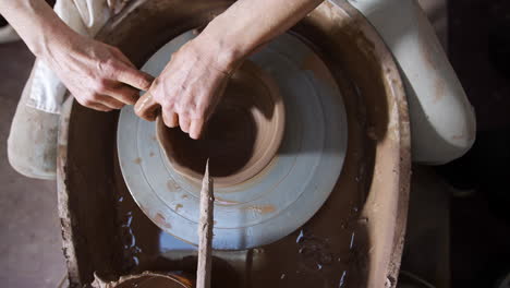 overhead close up of male potter shaping clay for bowl on pottery wheel in ceramics studio