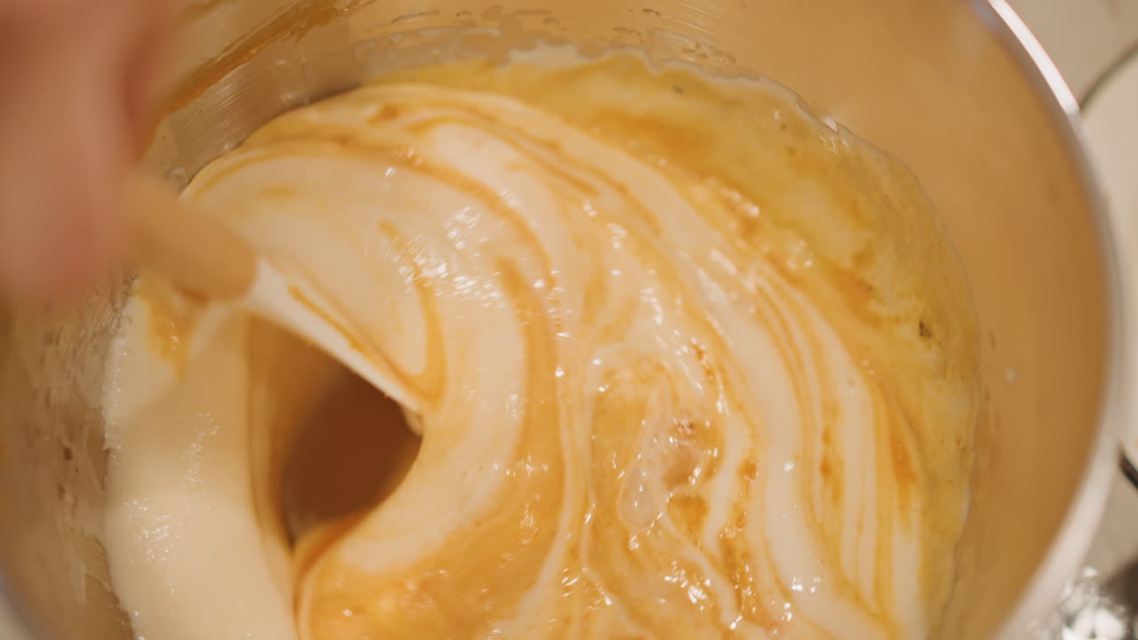 Folding meringue into pumpkin filling home baker gently folds airy egg whites into spiced pumpkin custard in stainless bowl with wooden spatula, soft warm light, swirls of cream and orange, intimate