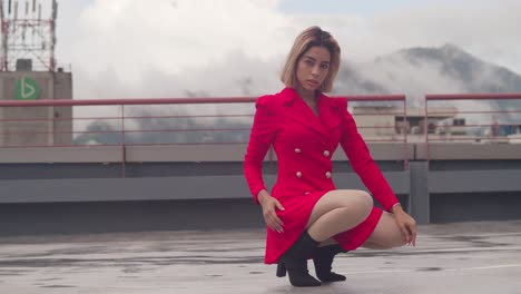 in the cityscape, a young girl of hispanic descent poses on a rooftop wearing a short red dress