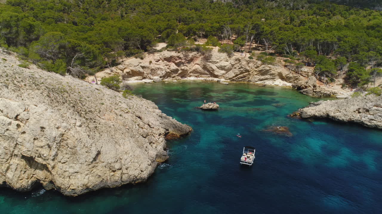 Droneoptagelse af en bugt på Mallorca med klipper og træer på en solrig dag, Spanien, flyver baglæns, 4K.