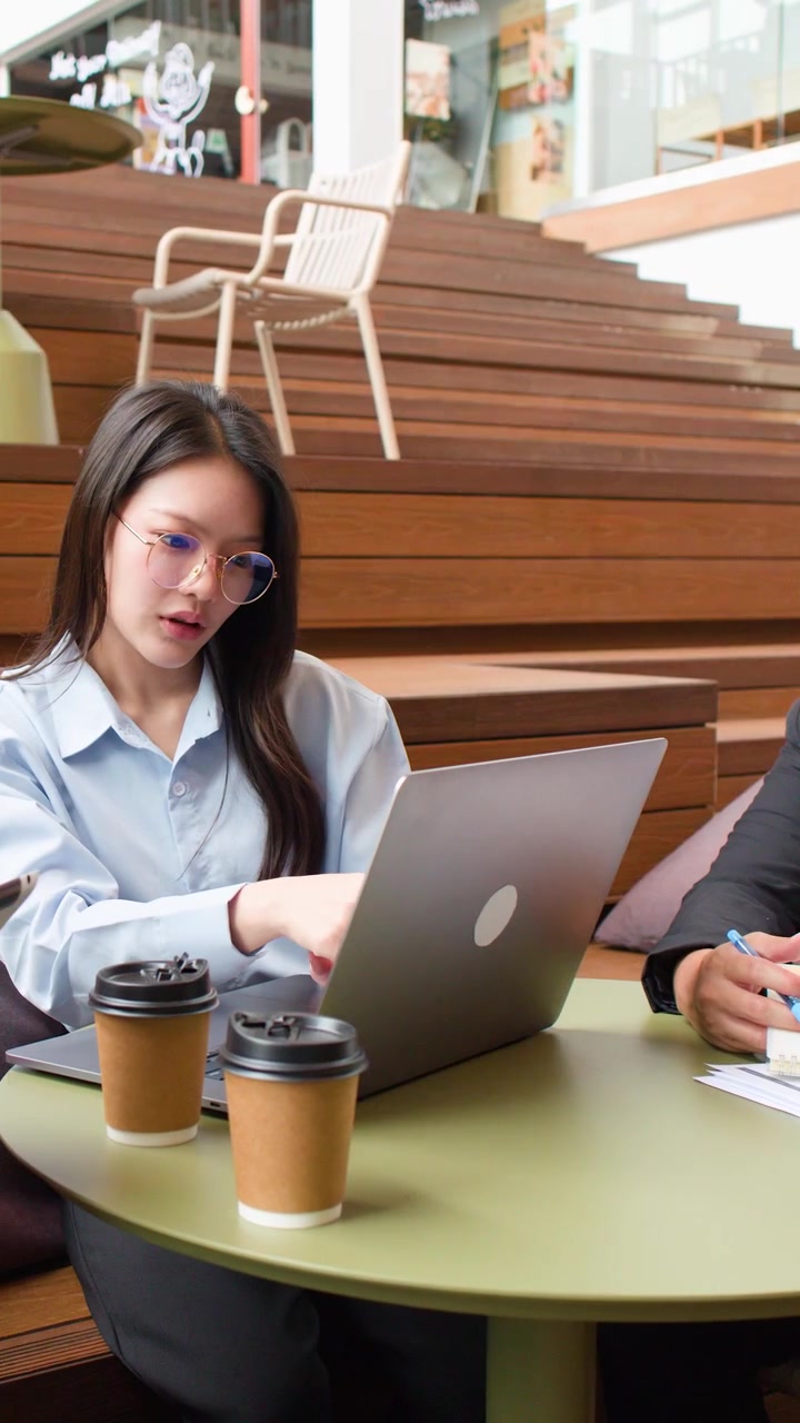 Diversi giovani professionisti aziendali asiatici discutono i dettagli del progetto utilizzando laptop e documenti in un moderno coworking.