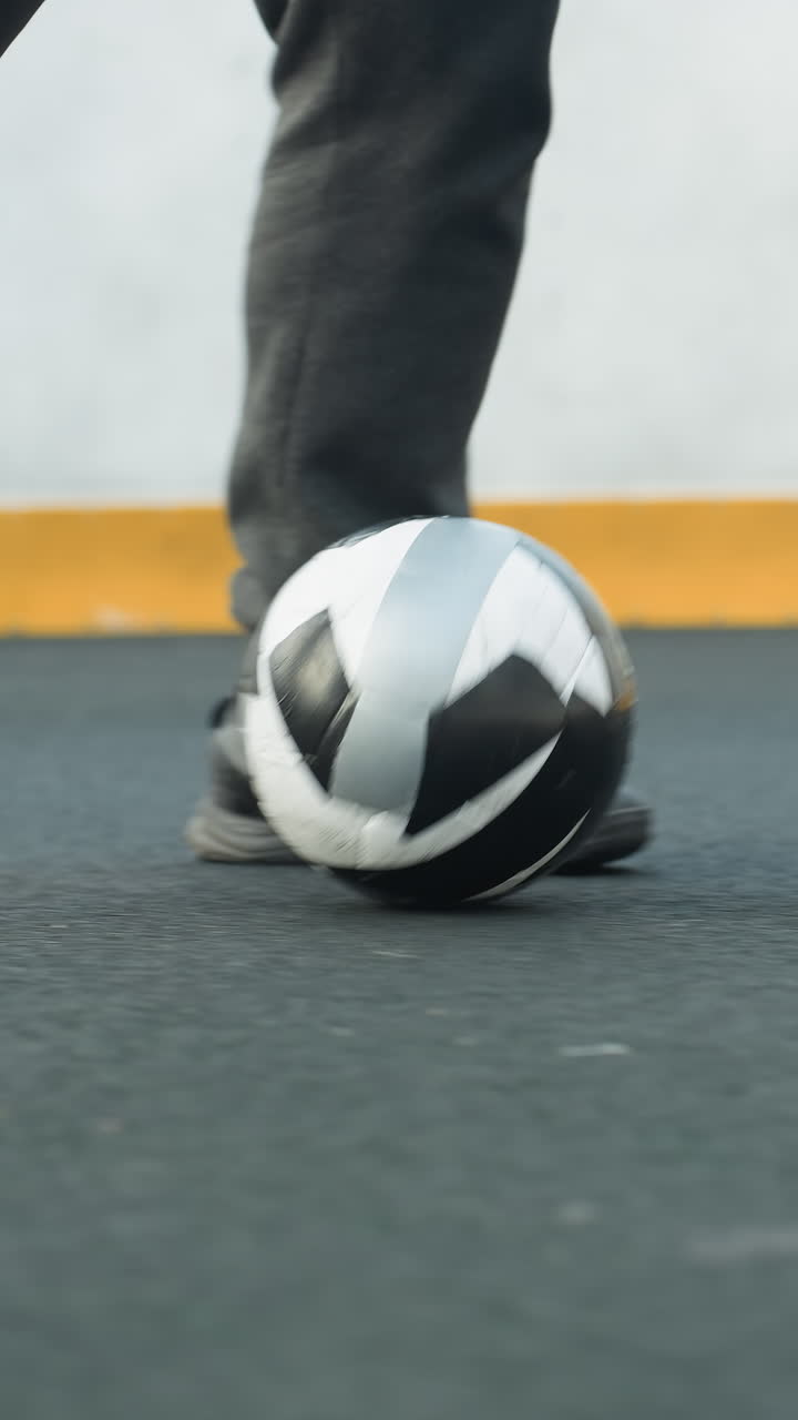 primer plano de un hombre controlando una pelota de fútbol con un trabajo de pies preciso en la arena deportiva, mostrando agilidad y habilidades atléticas, una vibrante barrera amarilla en el fondo