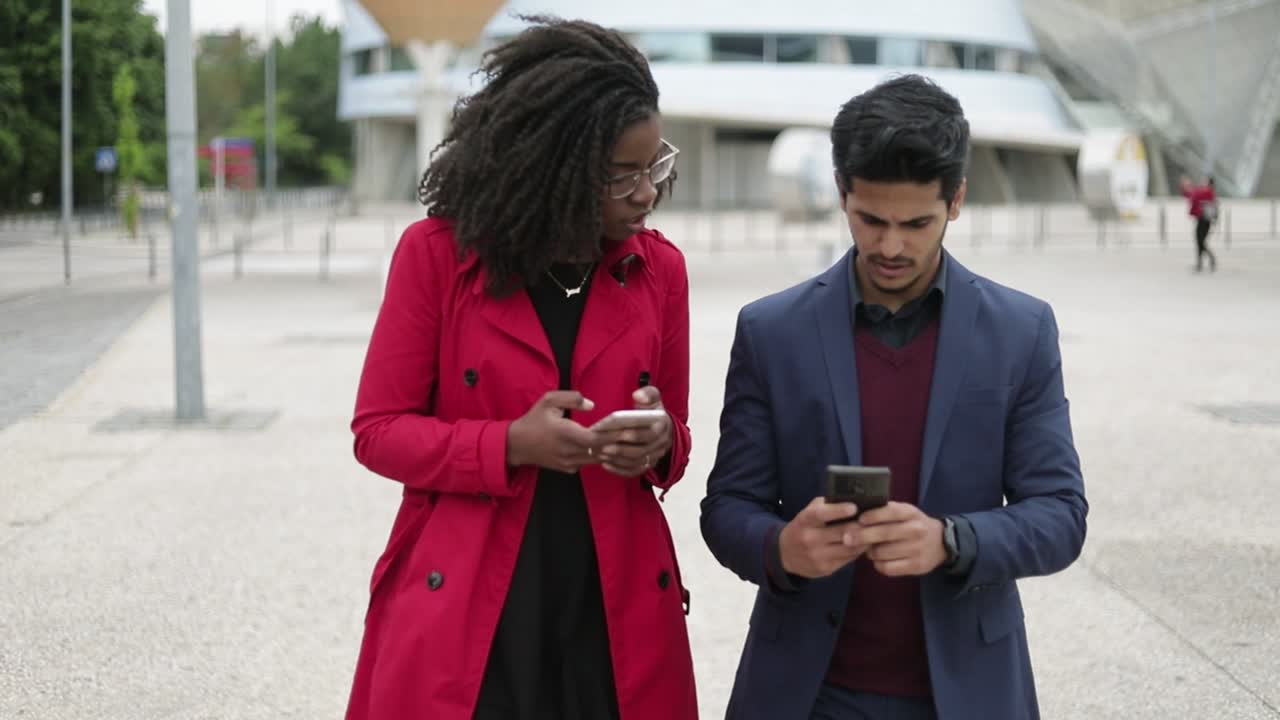 mujer y hombre caminando por la calle, hombre mostrando fotos en el teléfono