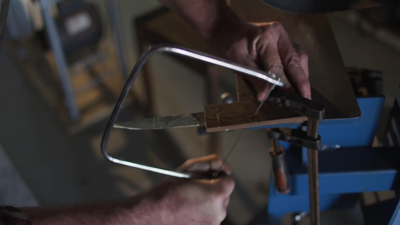cerca de las manos de un hombre caucásico fabricante de cuchillos en un taller usando una sierra