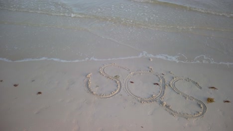 Static-shot-of-SOS-written-in-the-sand-on-a-beach