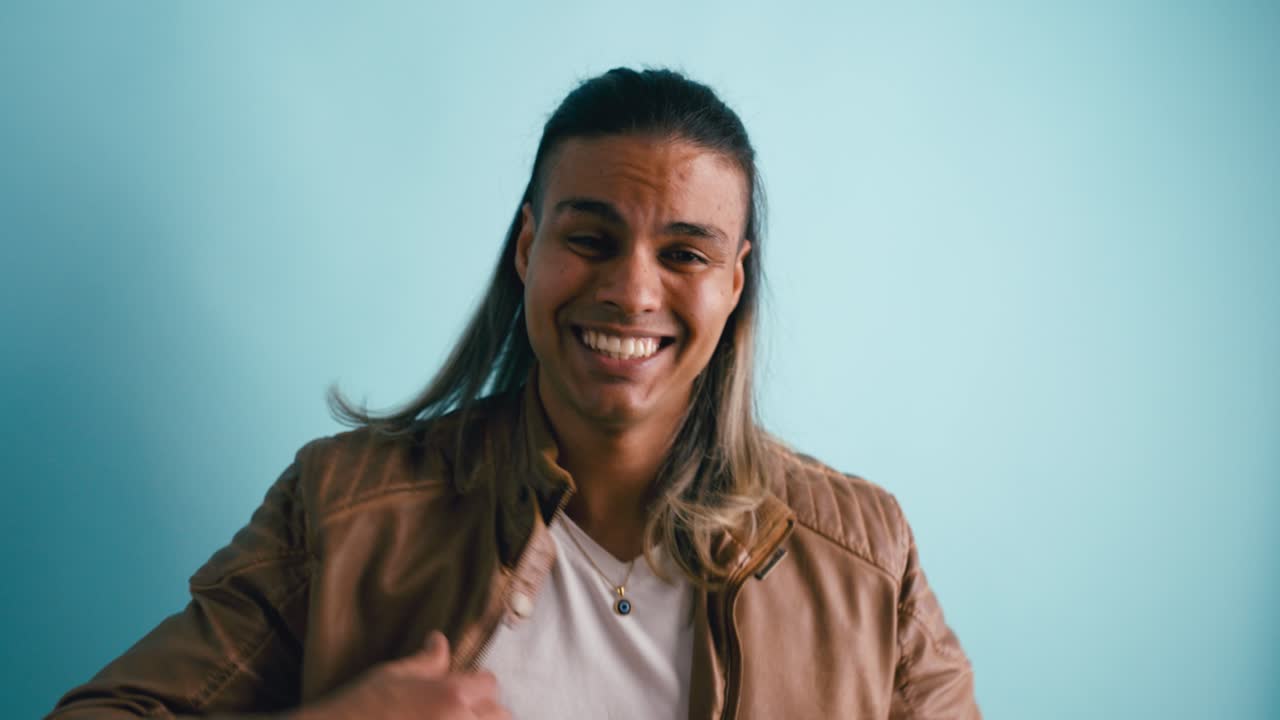 Giovane uomo giocoso con i capelli lunghi che sorride e fa gesti con le mani.