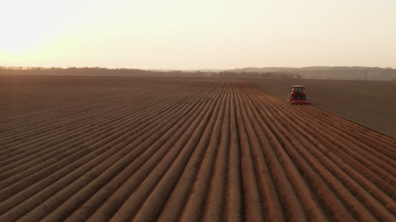 Trattore moderno che trascina un aratro creando solchi nel terreno in un campo sotto la luce del sole