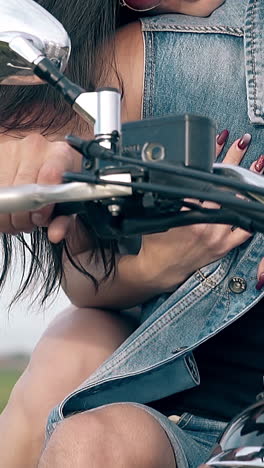 closeup girl with wristwatch and manicure hugs muscular man in denim vest sitting on black motorbike slow motion